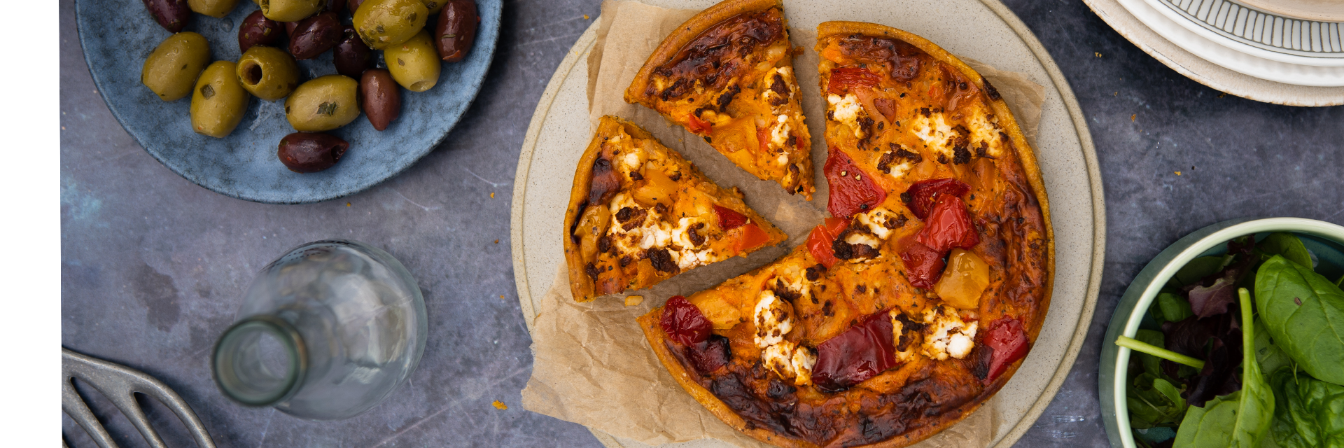 An image of a Higgidy Mediterranean Pepper Quiche on a table surrounded by other freshly prepared food.